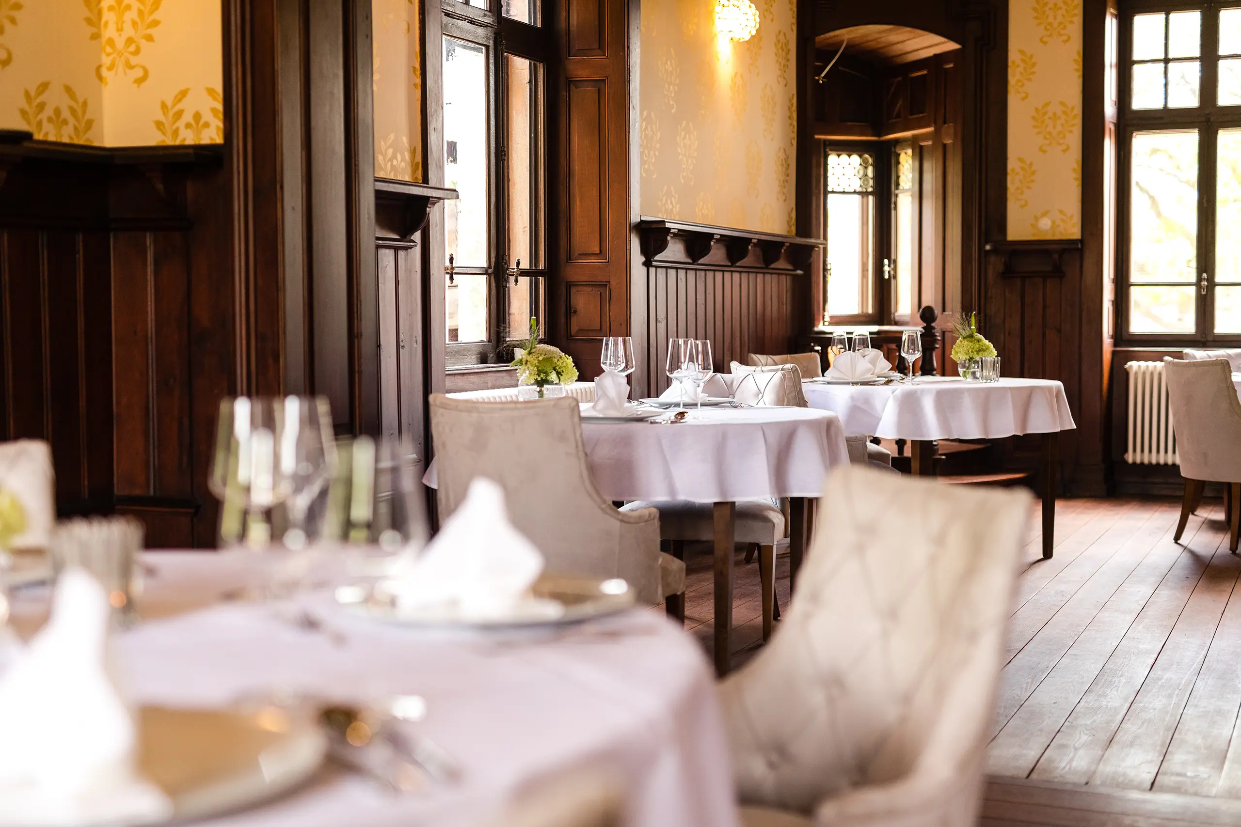 Eingedeckte Tische mit weißen Tischdecken im Restaurant Schlösschen mit Blick in den Garten