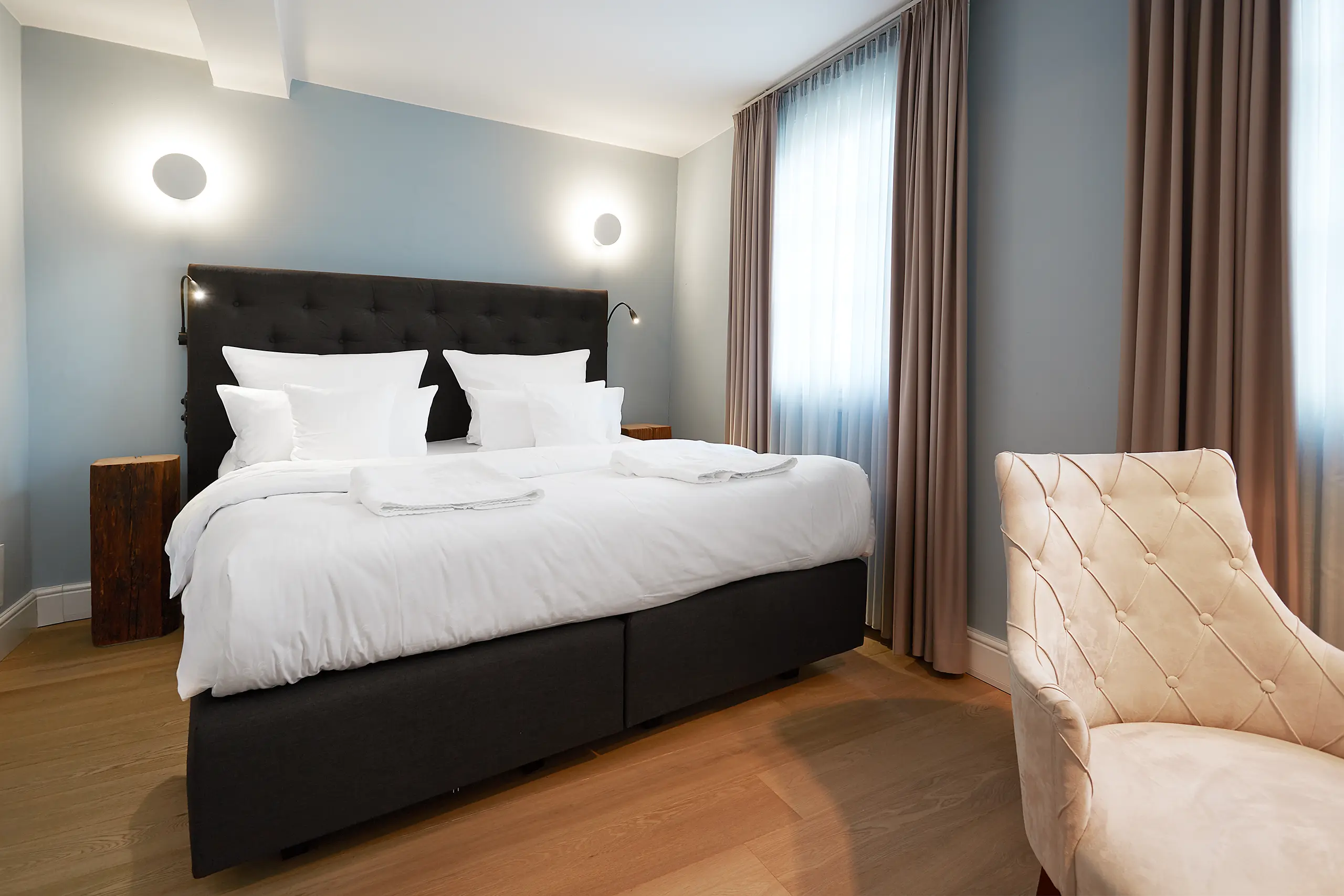 Fachwerkzimmer mit Doppelbett, weißem Sessel und Wandlampen