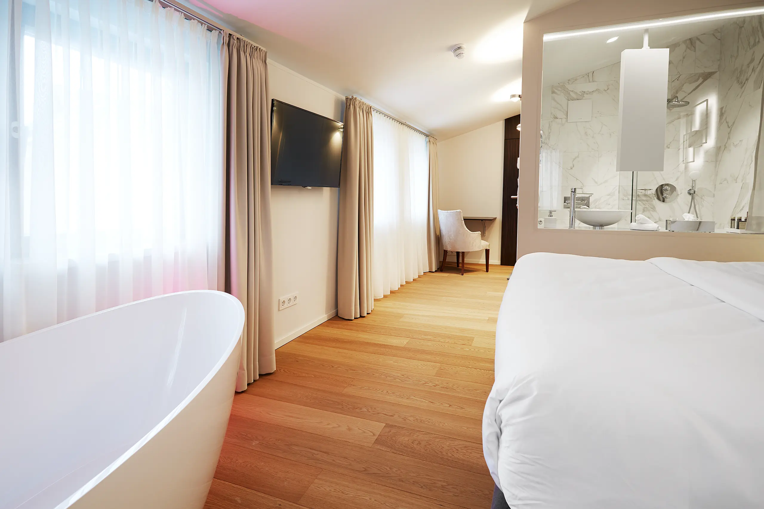 Honeymoon-Suite mit freistehender Badewanne neben dem Bett und Blick ins Bad