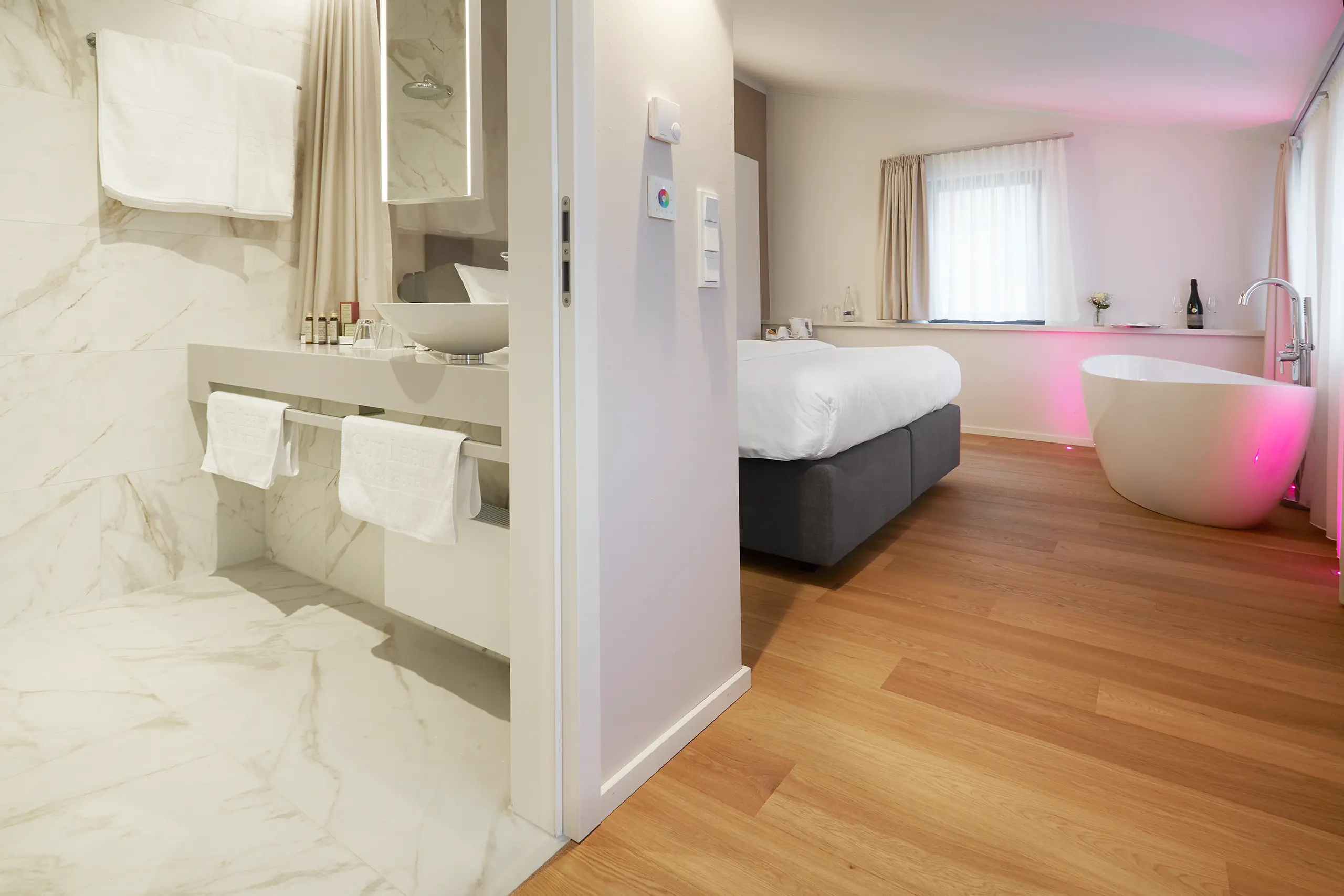 Honeymoon-Suite mit Doppelbett, Marmorwand und Badewanne in farbigem Licht