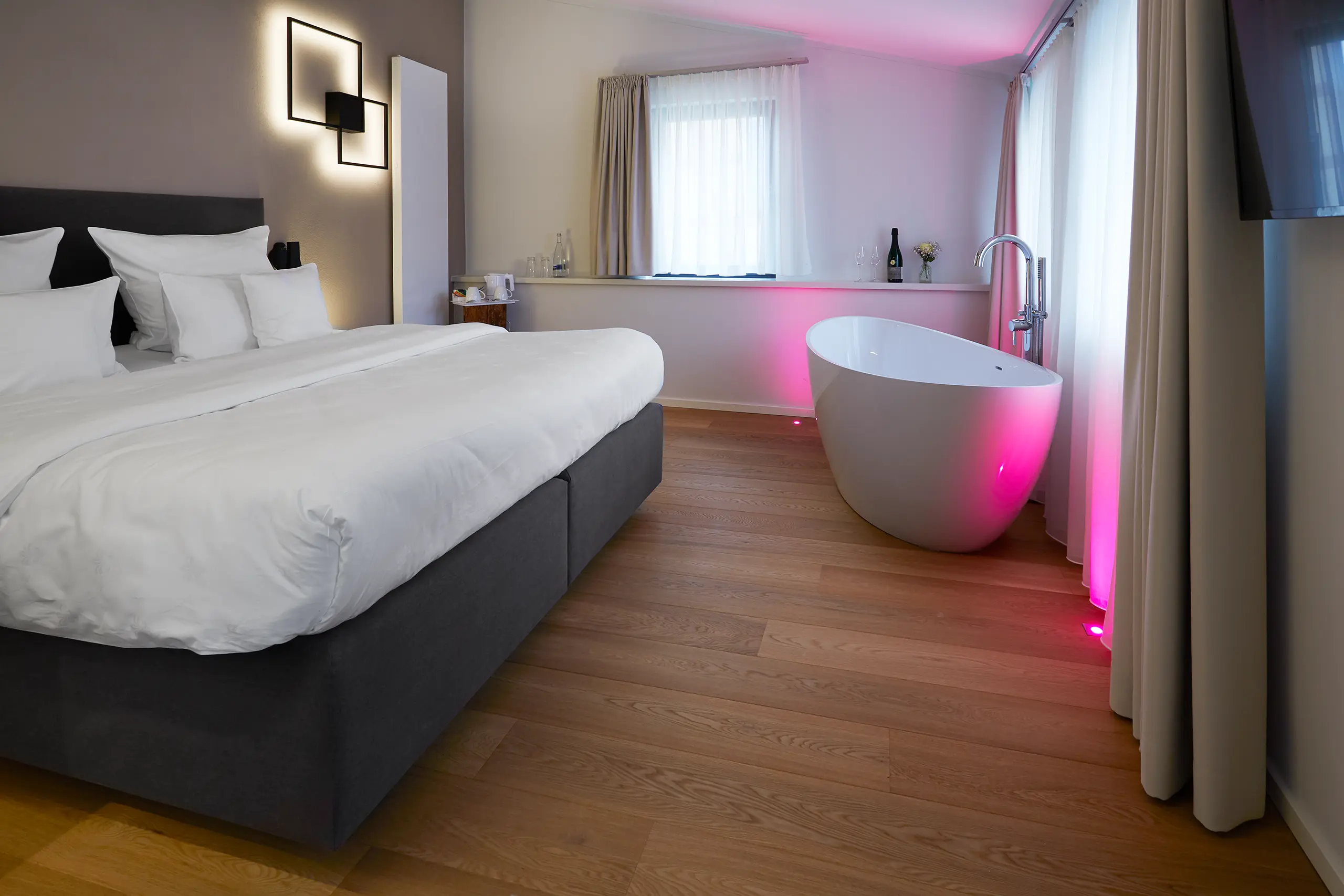 Honeymoon-Suite mit Doppelbett und freistehender Badewanne in rosa Licht