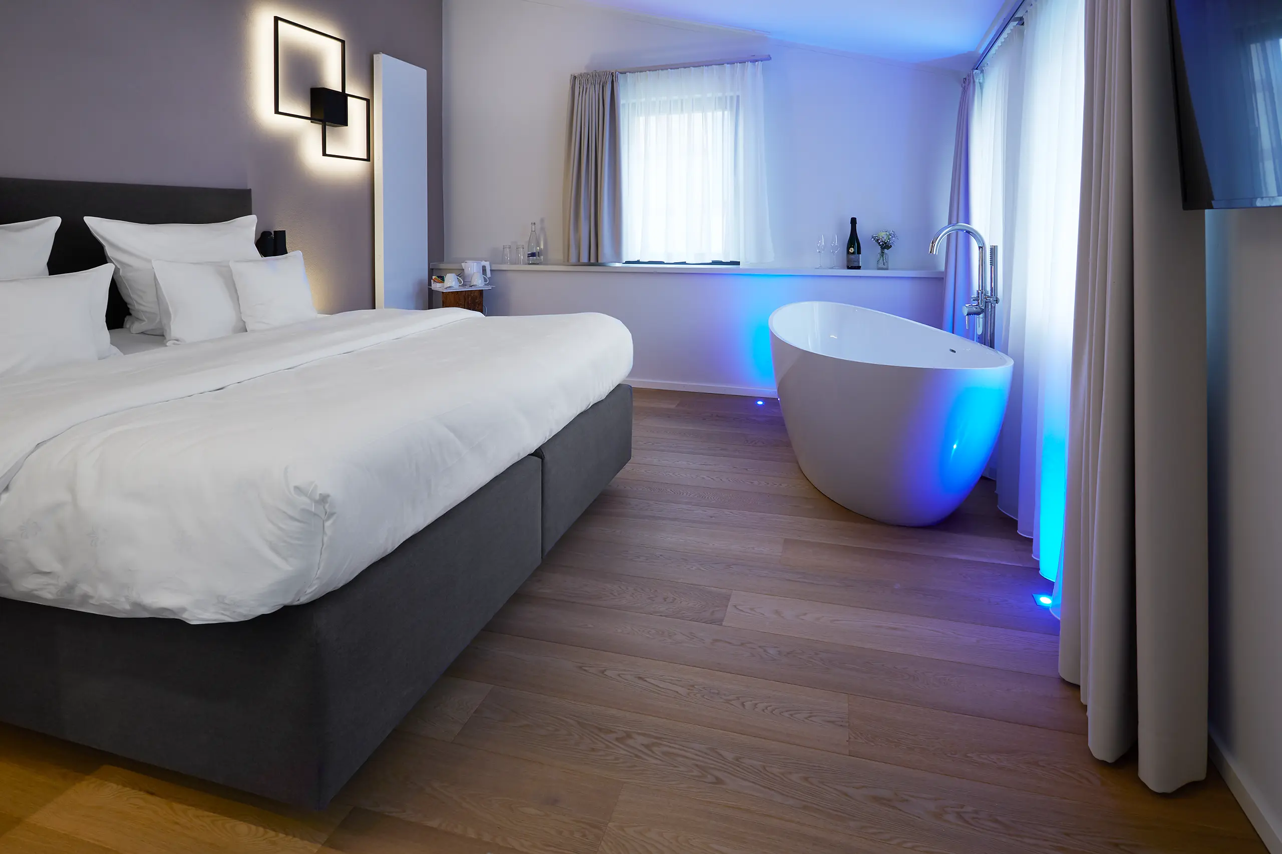 Honeymoon-Suite mit Doppelbett und Badewanne in blau-violettem Licht