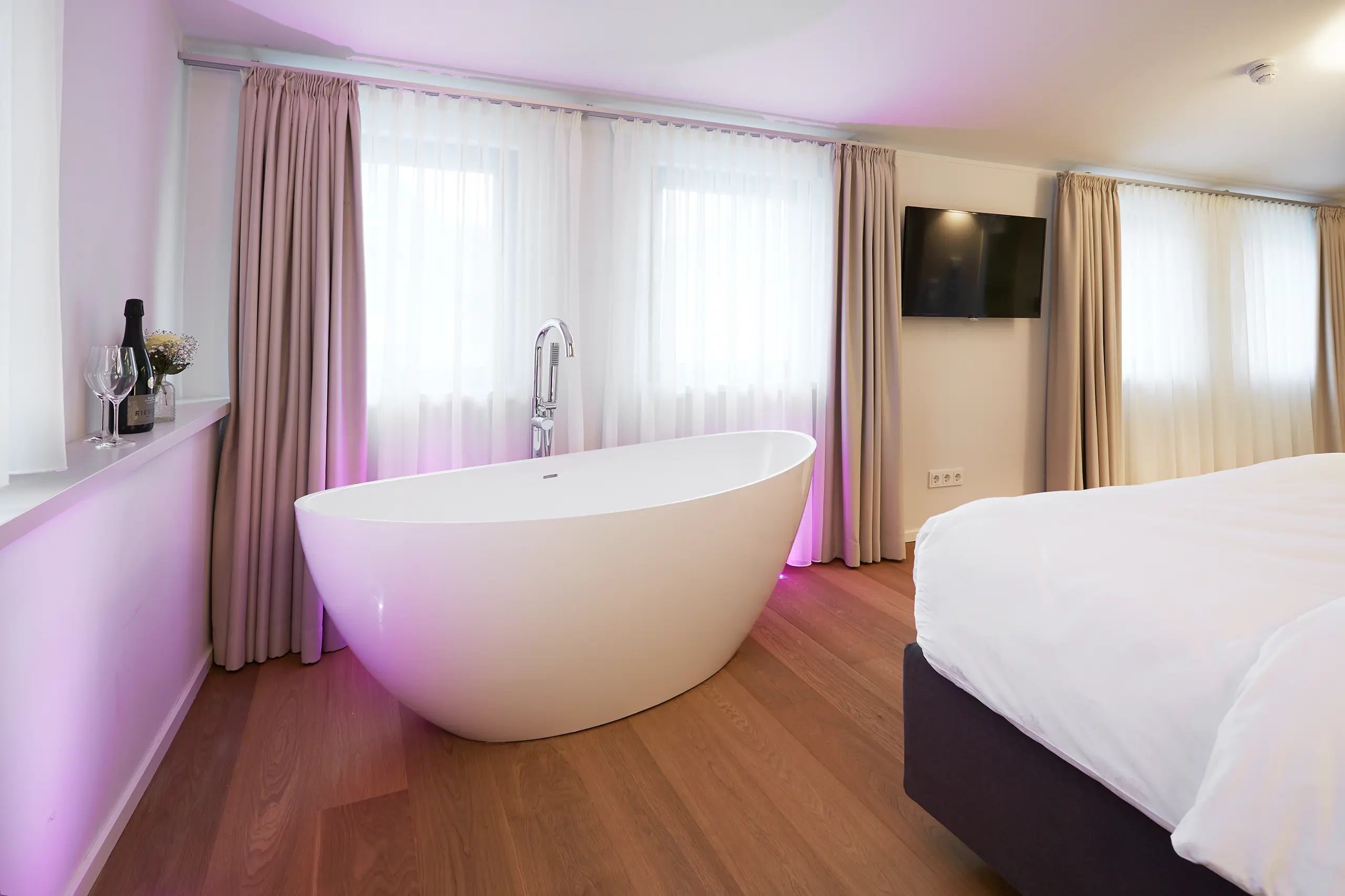 Freistehende Badewanne neben dem Bett in der Honeymoon-Suite in rosa Licht