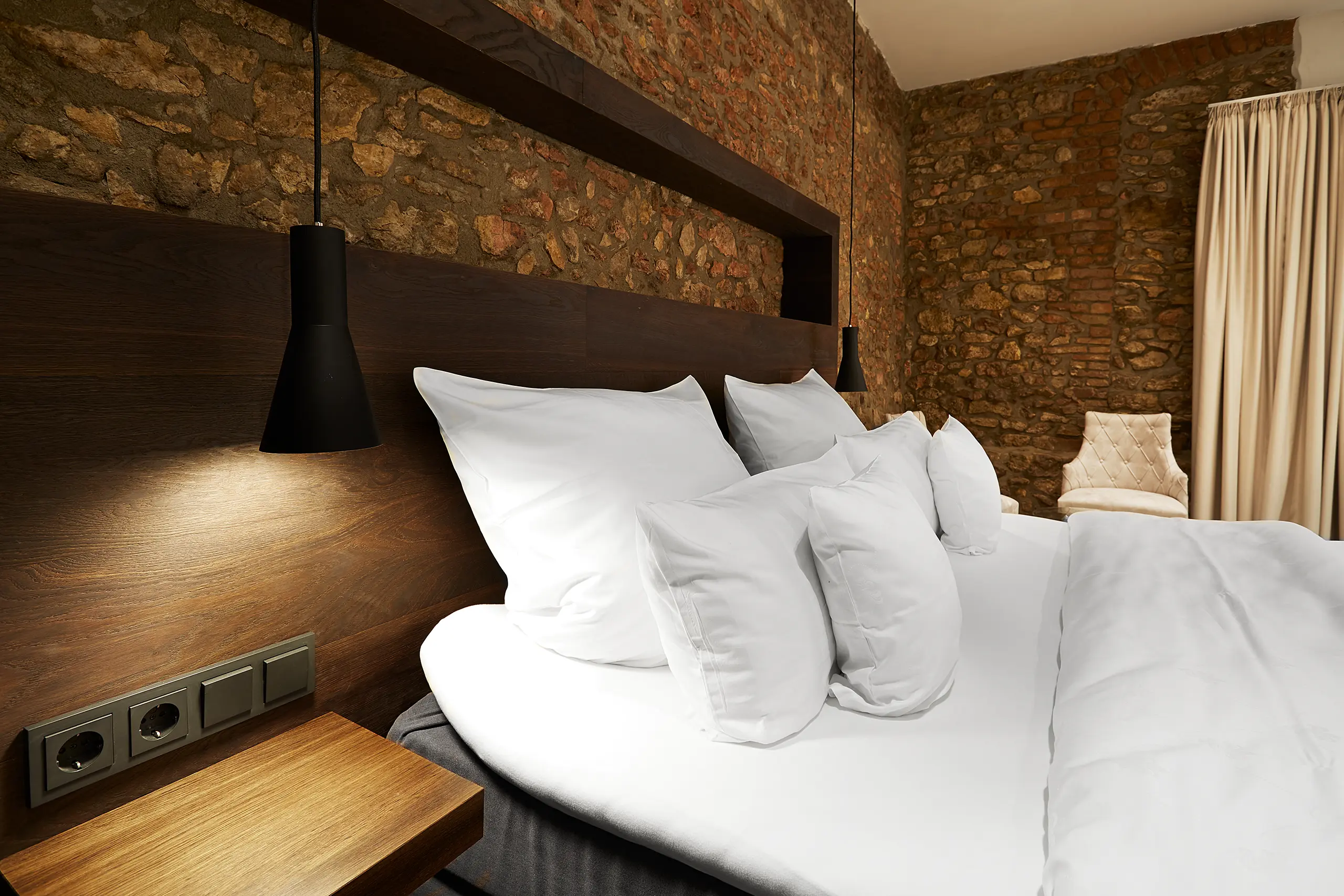 Doppelbett mit schwarzer Pendelleuchte vor Natursteinwand im barrierefreien Hotelzimmer Rheinhessen