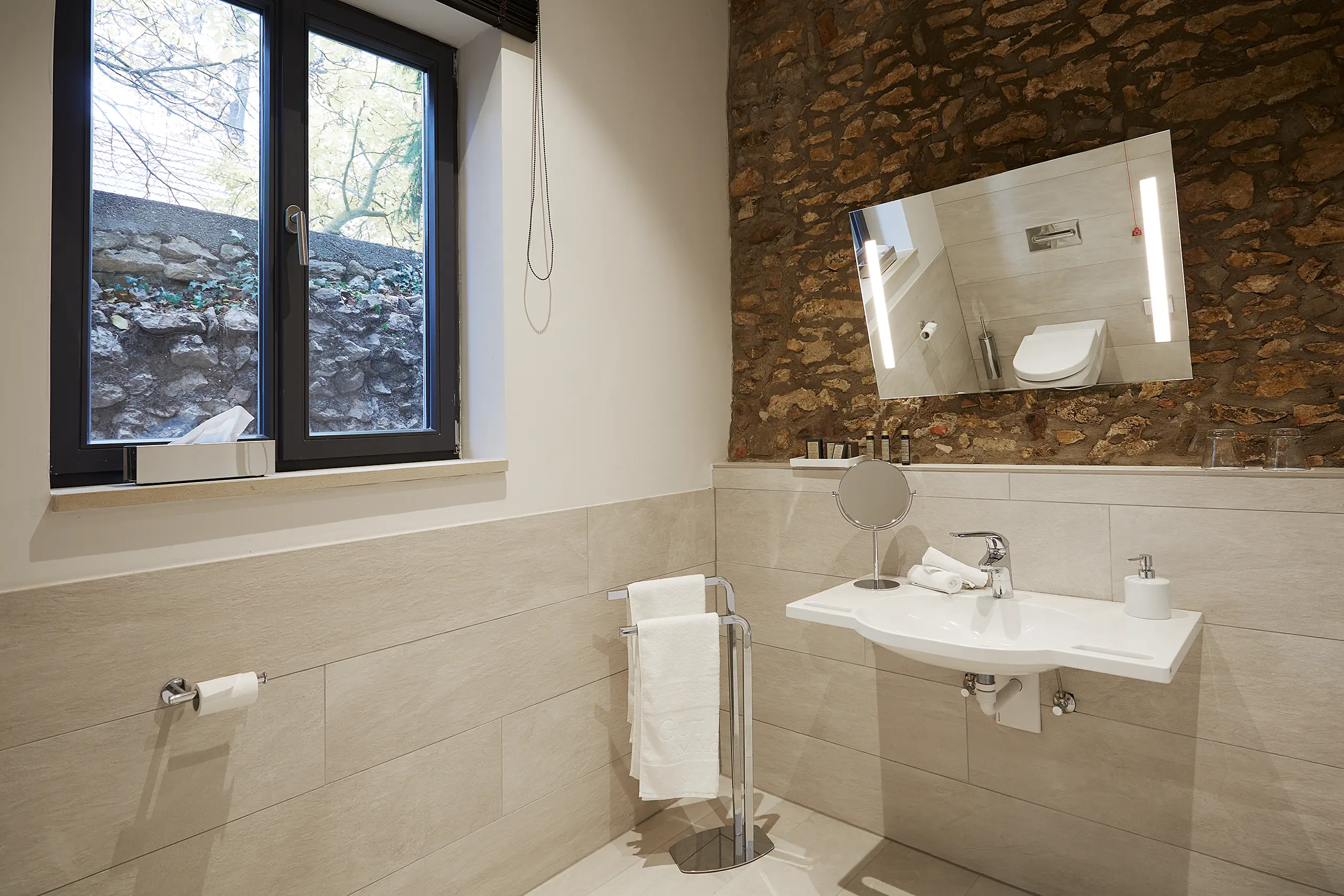 Badezimmer mit Waschtisch, Spiegel und Natursteinwand im barrierefreien Zimmer