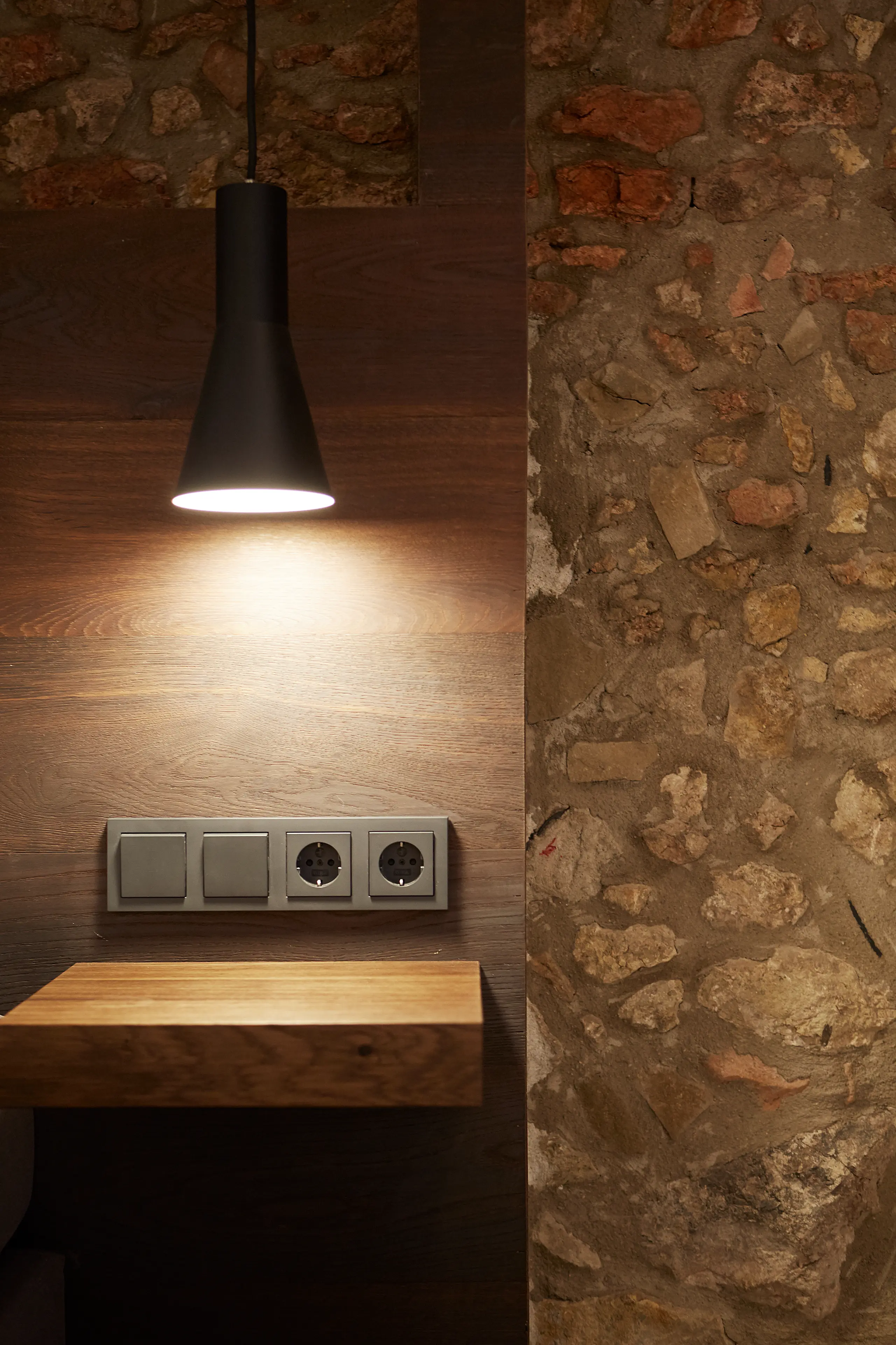 Nachttisch mit Pendelleuchte an der Natursteinwand im barrierefreien Zimmer