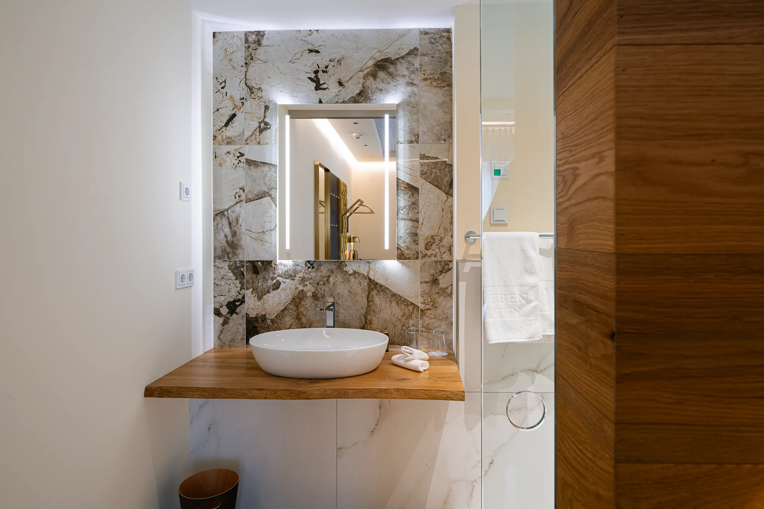 Badezimmer in Zimmer 21 im Neubau mit Marmorwand, Waschbecken und Spiegel