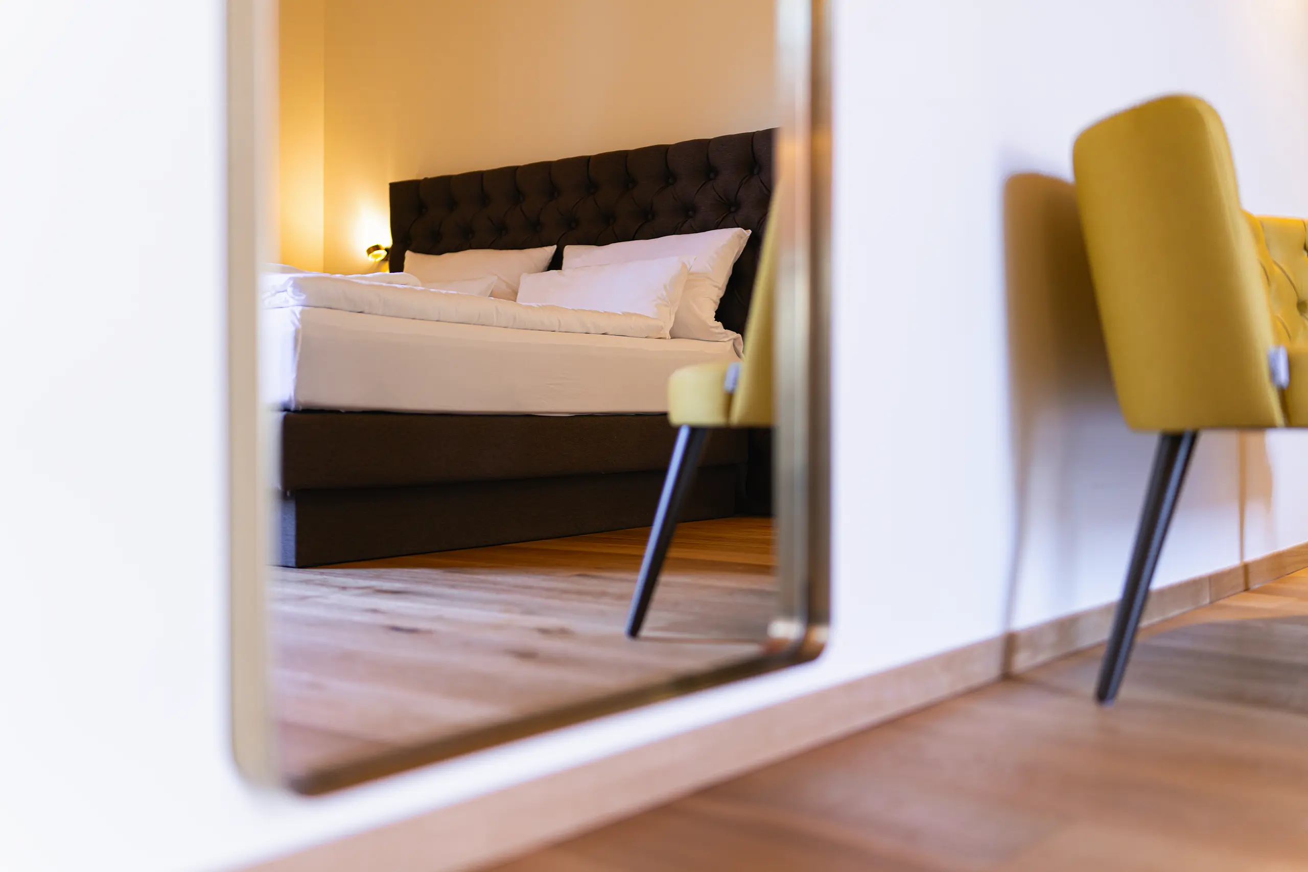 Spiegelansicht von Zimmer 28 im Neubau mit Bett und gelbem Sessel