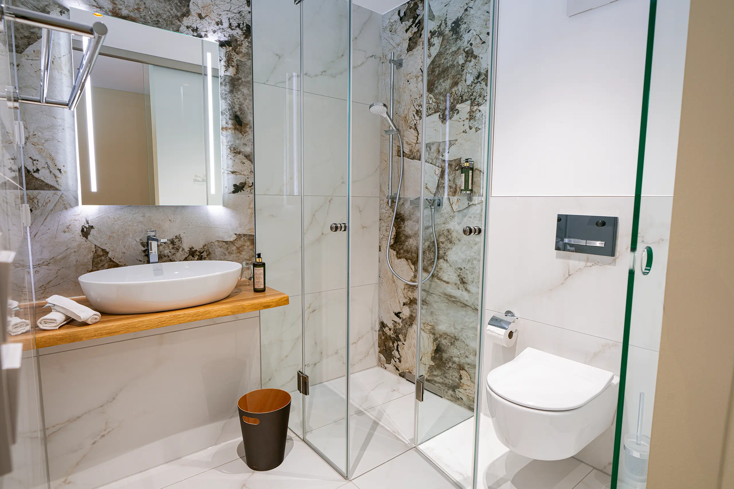 Badezimmer in Zimmer 35 im Neubau mit Waschbecken, Marmorwand und Glasdusche