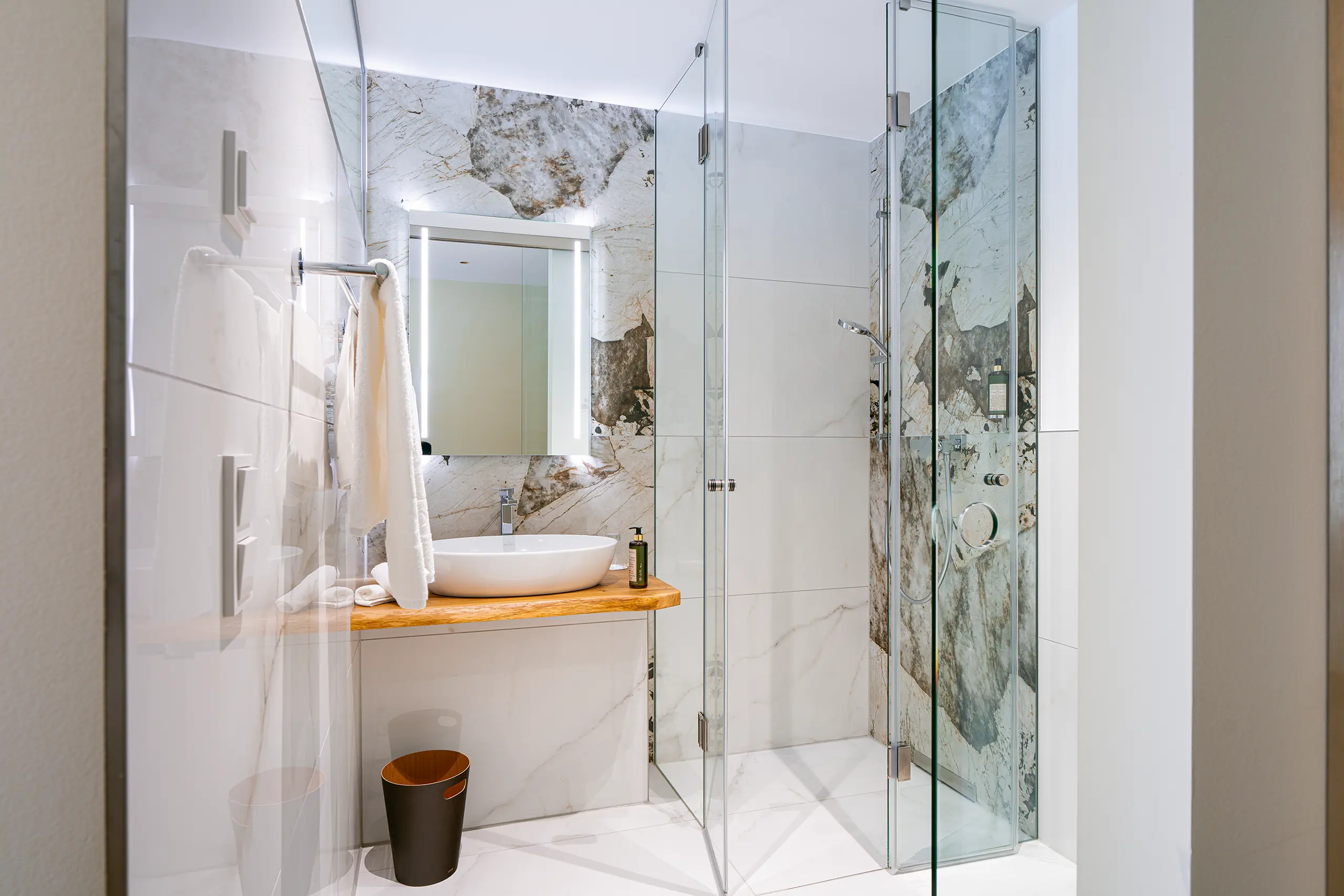 Badezimmer in Zimmer 37 im Neubau mit Marmorwand, Waschbecken und Glasdusche