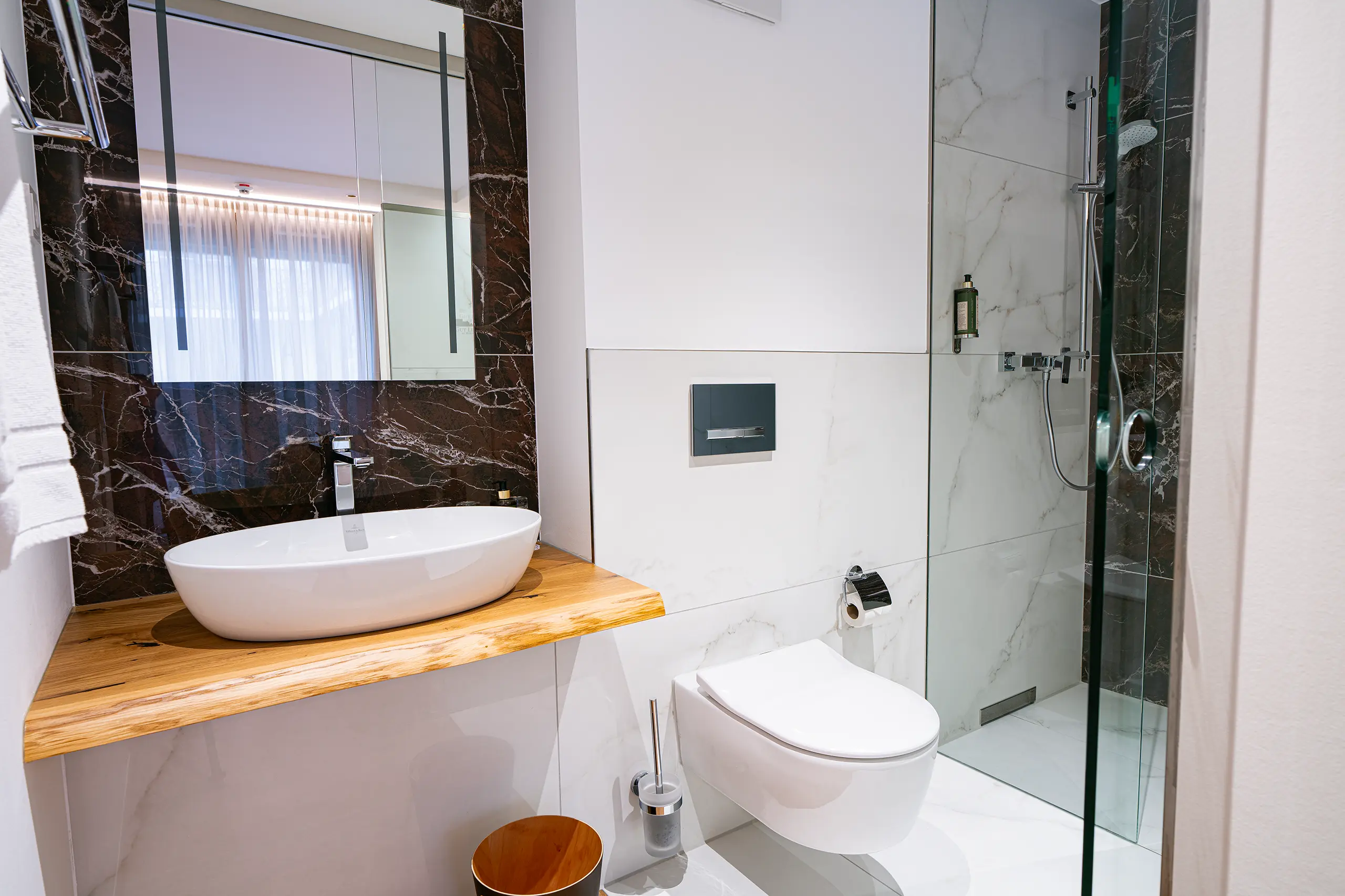 Badezimmer in Zimmer 38 im Neubau mit Waschbecken, dunkler Marmorwand und Dusche