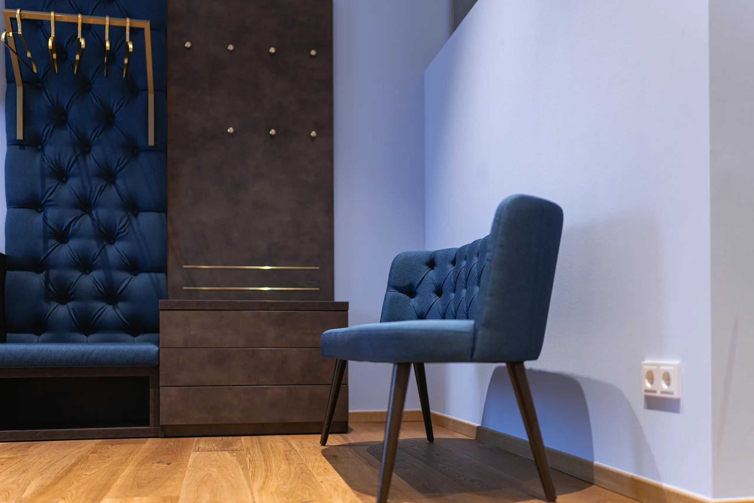 Blauer Sessel und gepolsterte Wand mit Kleiderhaken in Zimmer 40 im Neubau