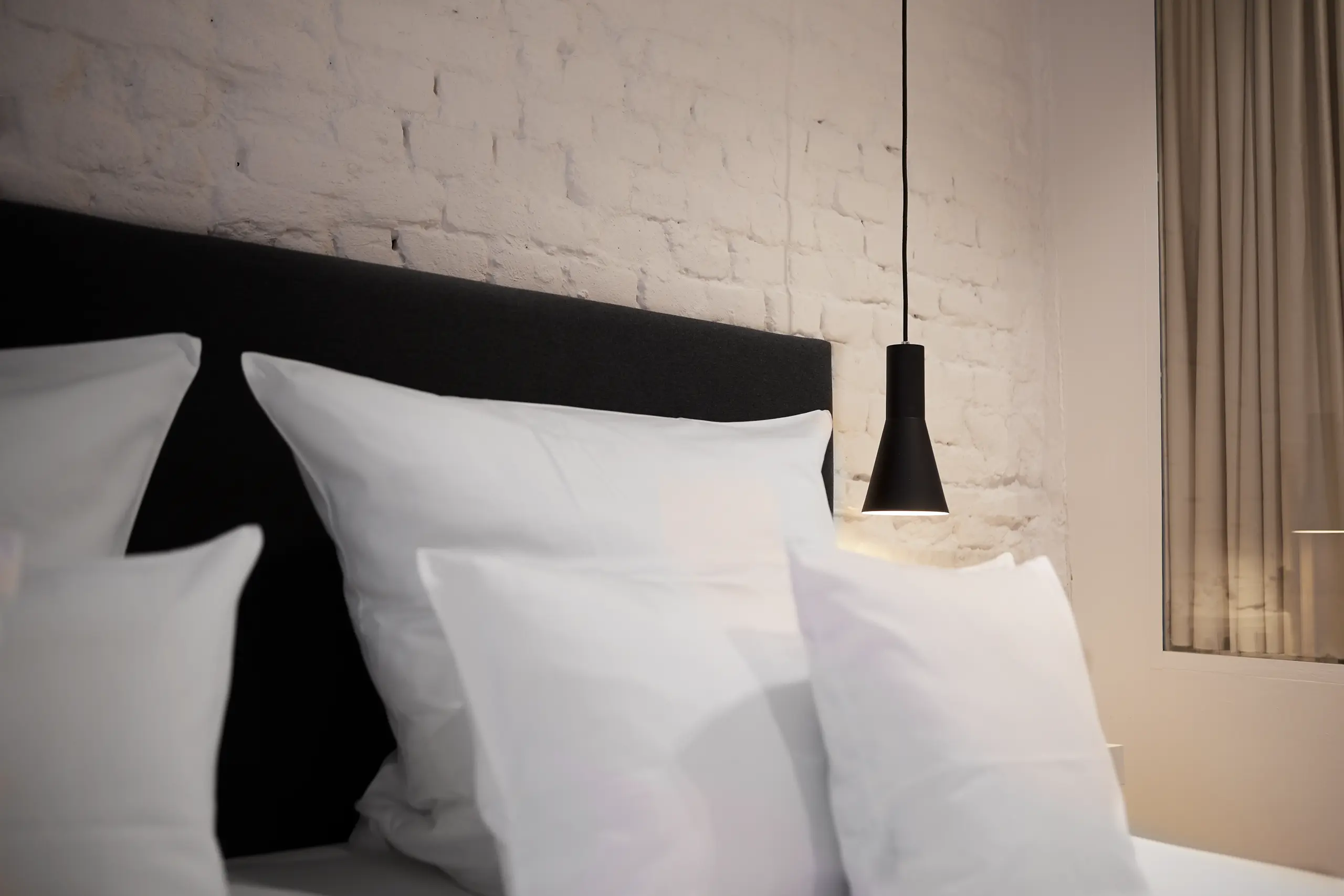 Doppelbett mit Kissen vor weißer Backsteinwand im Superior-Zimmer in der Scheune