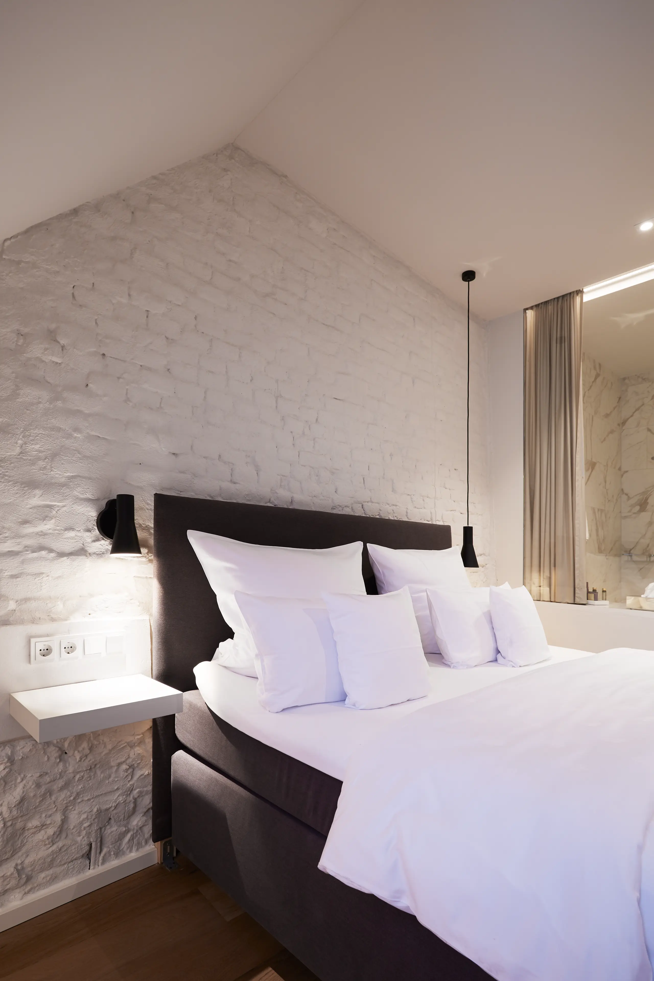 Doppelbett unter der Dachschräge mit weißer Backsteinwand im Superior-Zimmer in der Scheune