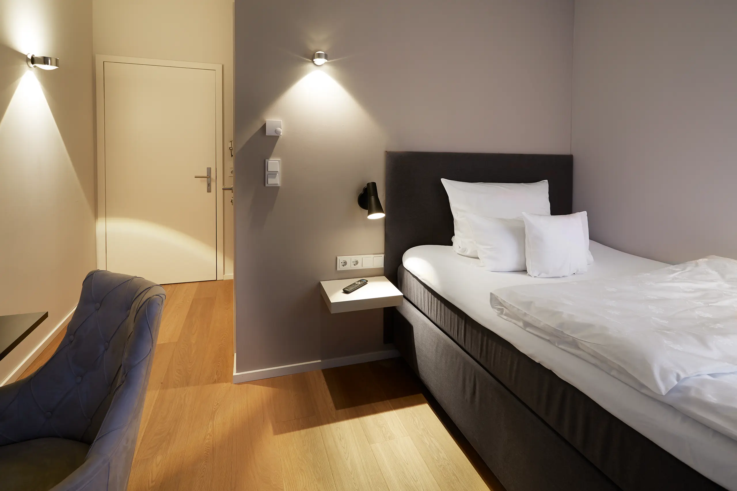Einzelzimmer Standard in der Remise mit Bett, Wandleuchten und Blick ins Bad