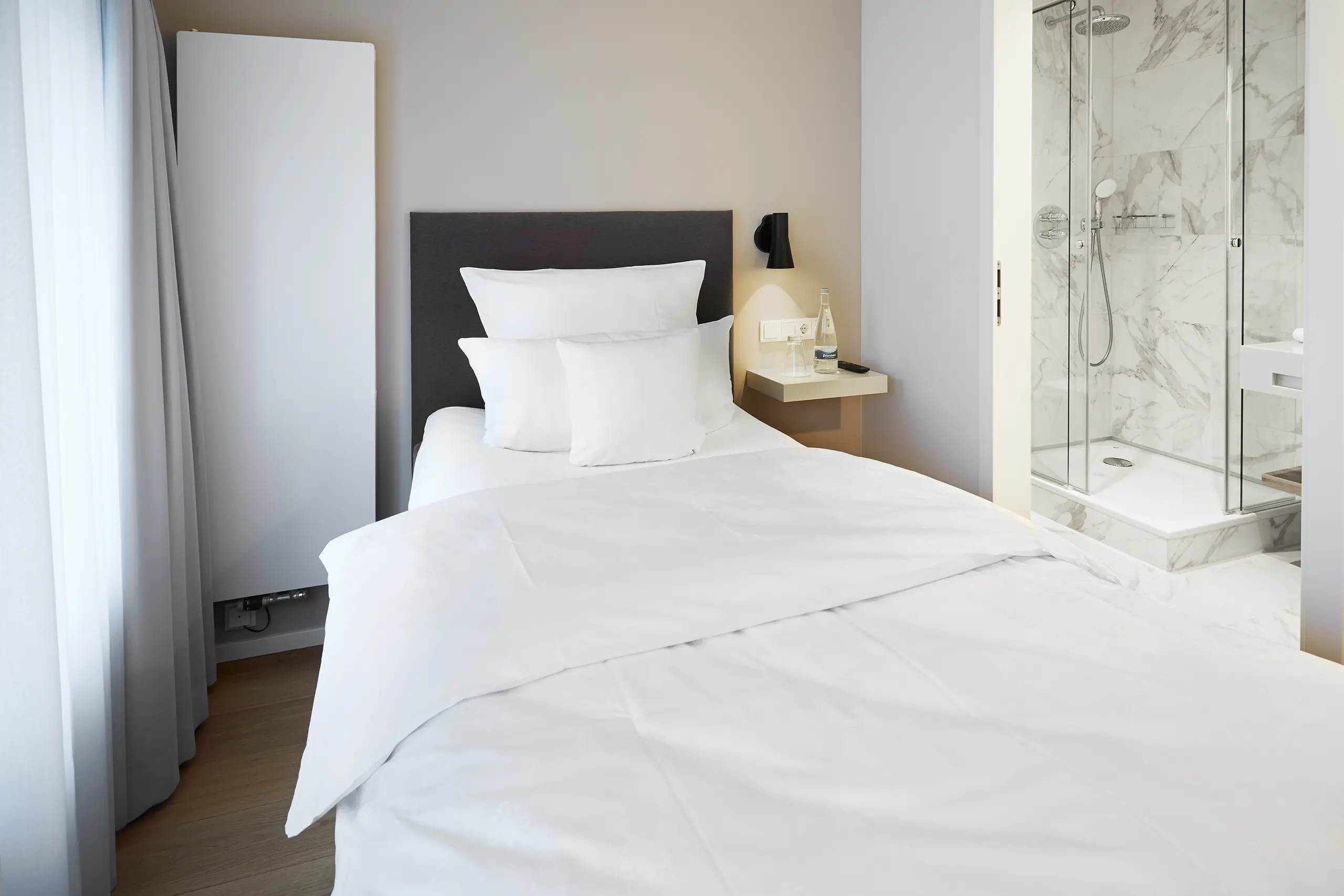 Einzelbett mit weißer Bettwäsche vor dunklem Kopfteil im Einzelzimmer in der Remise