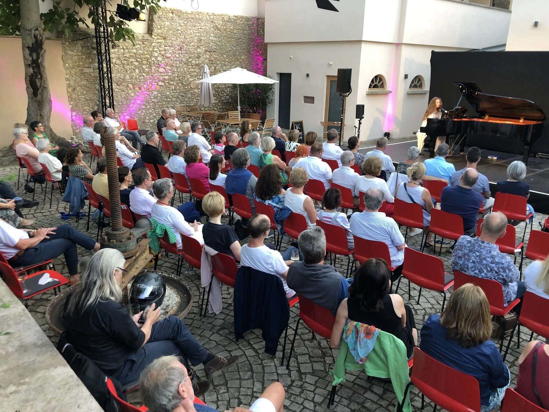 Publikum auf roten Stühlen bei einem Konzert im Innenhof von Gut Leben am Morstein