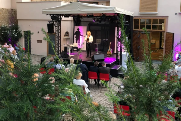 Konzert im Innenhof mit Sängerin auf der Bühne und Publikum an Tischen